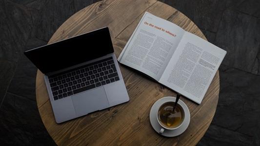 A computer, a book and a cup of coffee on a round table